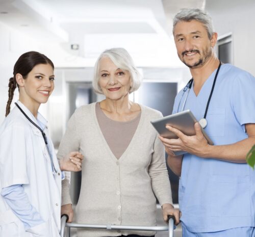 Portrait of male and female physiotherapists standing with female patient using walker at rehab center