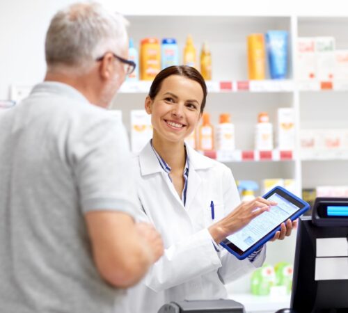 medicine, healthcare and technology concept - happy apothecary and senior male customer with digital prescription on tablet pc computer screen at pharmacy
